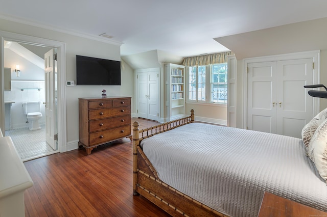 bedroom featuring two closets, crown molding, connected bathroom, wood-type flooring, and baseboards