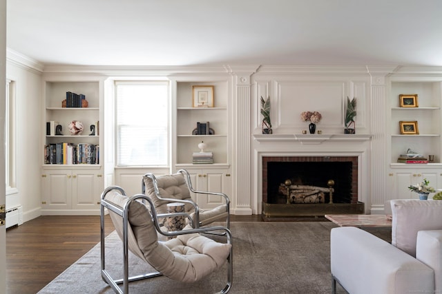 living room with a baseboard heating unit, ornamental molding, dark wood-type flooring, built in features, and a fireplace