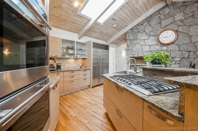 kitchen featuring appliances with stainless steel finishes, dark stone countertops, light wood-type flooring, vaulted ceiling with skylight, and sink