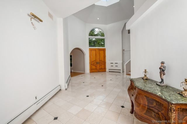 foyer entrance featuring a towering ceiling, a skylight, baseboard heating, and light tile patterned floors