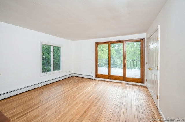 empty room featuring light hardwood / wood-style flooring, baseboard heating, and a healthy amount of sunlight