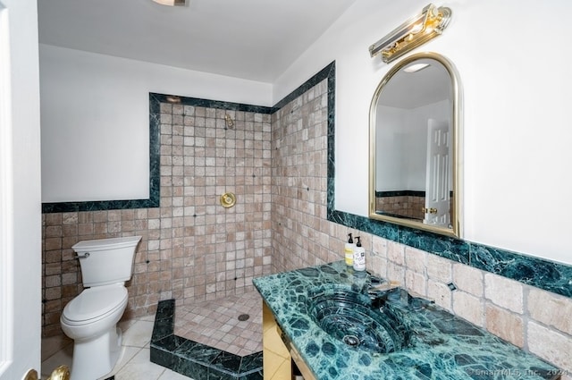 bathroom featuring vanity, a tile shower, tile patterned floors, tile walls, and toilet