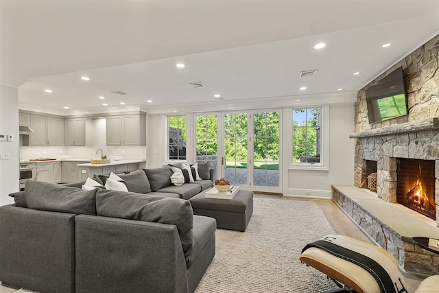 living room with light hardwood / wood-style floors, a stone fireplace, and ornamental molding