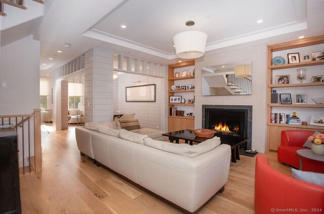 living room with a tray ceiling, built in features, ornamental molding, and light hardwood / wood-style floors