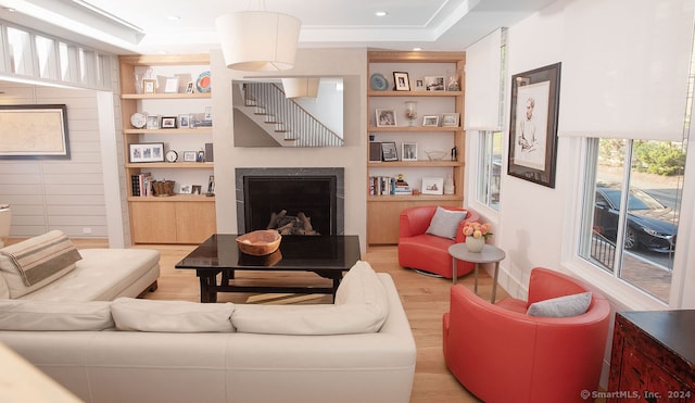 living room featuring built in shelves, a tray ceiling, hardwood / wood-style flooring, and ornamental molding