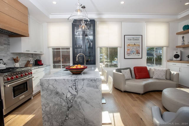 kitchen with custom range hood, light hardwood / wood-style flooring, white cabinetry, designer stove, and a center island with sink