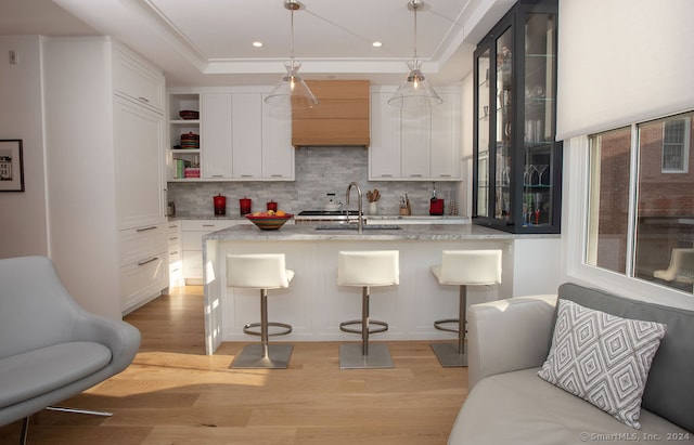 kitchen with hanging light fixtures, light hardwood / wood-style flooring, light stone counters, sink, and a kitchen bar