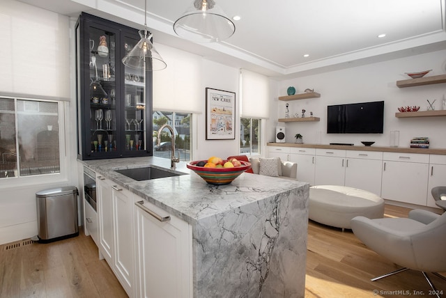 bar featuring light stone counters, sink, light wood-type flooring, and white cabinetry