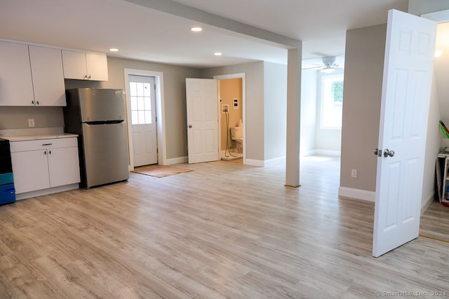 kitchen with black stove, stainless steel fridge, ceiling fan, white cabinets, and light hardwood / wood-style floors