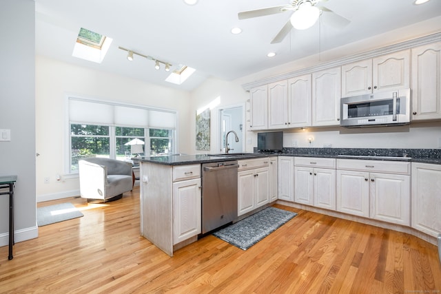 kitchen featuring a skylight, sink, kitchen peninsula, appliances with stainless steel finishes, and light wood-type flooring