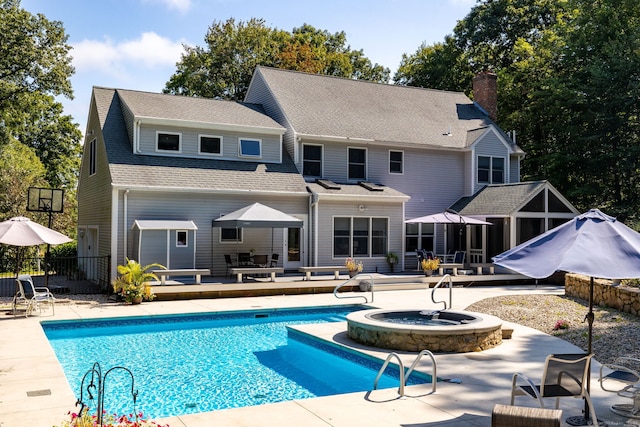 rear view of property with a swimming pool with hot tub and a patio