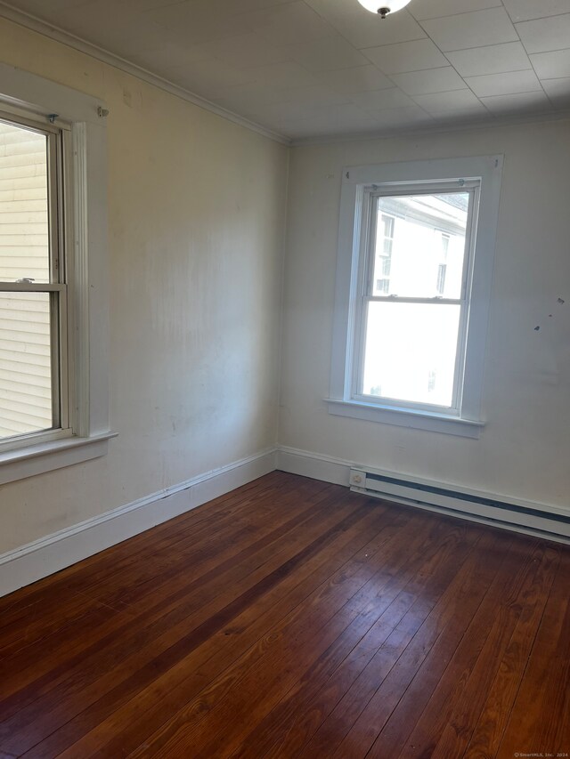 empty room with dark wood-type flooring, crown molding, and a baseboard heating unit