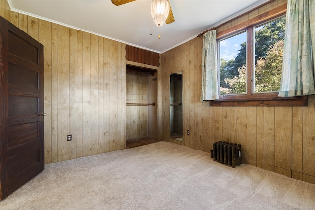 unfurnished room featuring carpet flooring, ceiling fan, radiator, and wooden walls