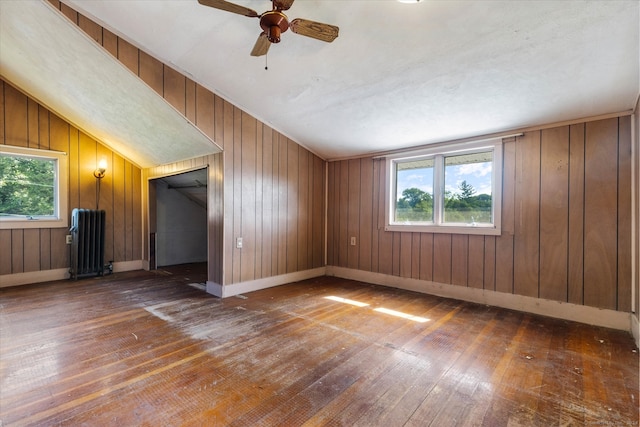 empty room with vaulted ceiling, wood walls, dark wood-type flooring, ceiling fan, and radiator heating unit