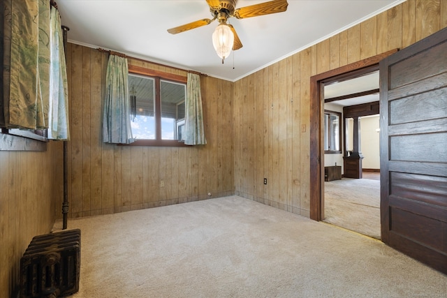 carpeted empty room featuring ceiling fan, wooden walls, and ornamental molding