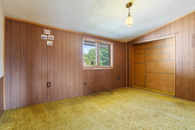 unfurnished bedroom featuring a closet, vaulted ceiling, wood walls, and carpet