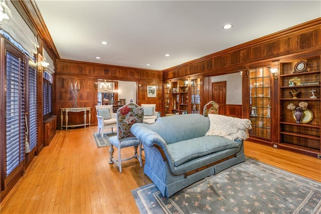 living room with ornamental molding, built in features, wood walls, and light hardwood / wood-style floors