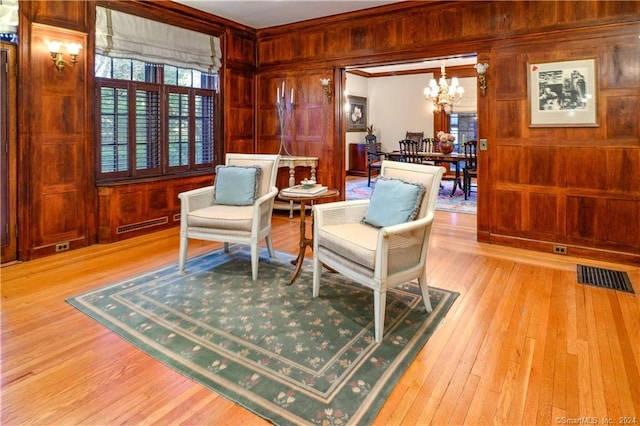 sitting room featuring light hardwood / wood-style flooring, wood walls, and a chandelier