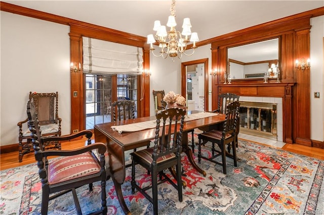 dining room featuring a fireplace, crown molding, a notable chandelier, and light hardwood / wood-style flooring