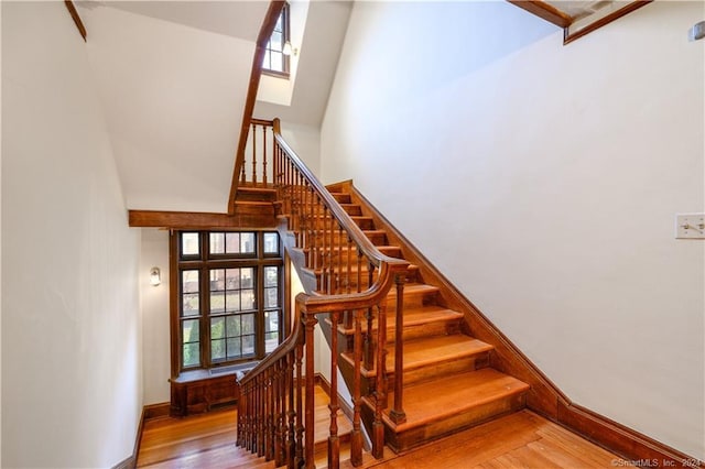 staircase with a towering ceiling, a healthy amount of sunlight, and wood-type flooring