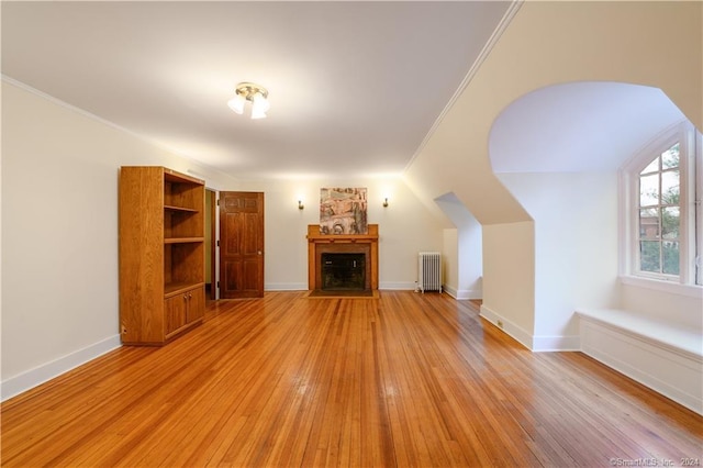 unfurnished living room featuring radiator heating unit, crown molding, light hardwood / wood-style flooring, and lofted ceiling