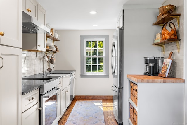 kitchen featuring wood-type flooring, wood counters, tasteful backsplash, white cabinets, and appliances with stainless steel finishes