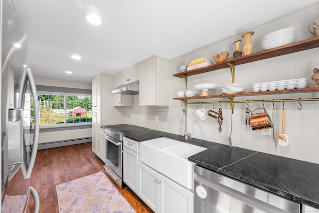 kitchen with dark wood-type flooring, tasteful backsplash, white cabinets, a baseboard radiator, and stainless steel appliances