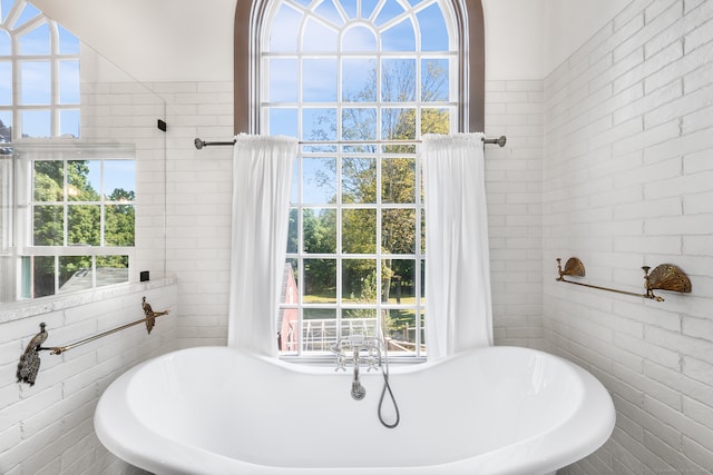 bathroom featuring a healthy amount of sunlight, brick wall, and a tub