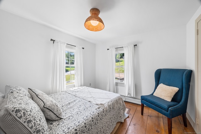 bedroom with a baseboard radiator, hardwood / wood-style floors, and multiple windows