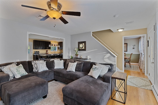 living room featuring ceiling fan, a textured ceiling, light wood-type flooring, and baseboard heating