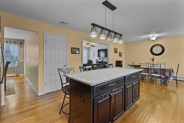 kitchen featuring hanging light fixtures, light hardwood / wood-style floors, a kitchen bar, a center island, and ceiling fan