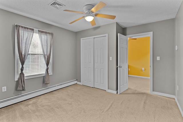 unfurnished bedroom featuring baseboard heating, a closet, a textured ceiling, ceiling fan, and light carpet