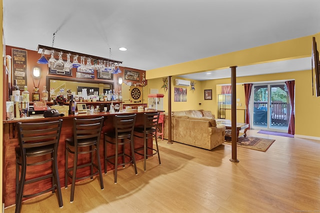 bar with light wood-type flooring and a wall mounted air conditioner