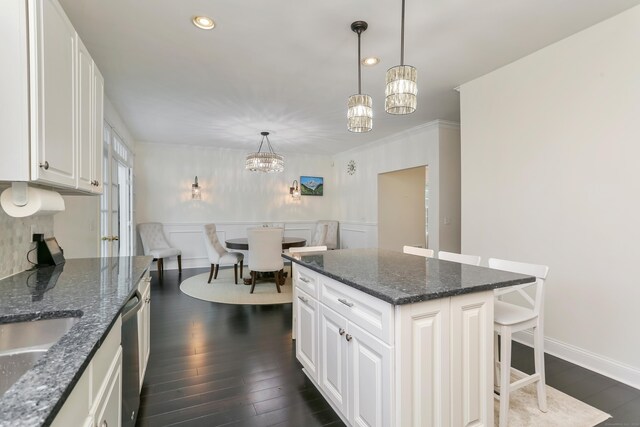 kitchen with dark stone countertops, an inviting chandelier, decorative light fixtures, dark wood-type flooring, and a kitchen island