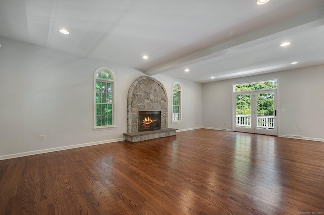 unfurnished living room with dark wood-type flooring, a stone fireplace, beam ceiling, and a wealth of natural light