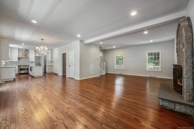 unfurnished living room featuring sink, hardwood / wood-style floors, beam ceiling, a notable chandelier, and a stone fireplace