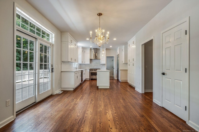 kitchen with high end stainless steel range oven, hanging light fixtures, white cabinets, decorative backsplash, and wall chimney exhaust hood