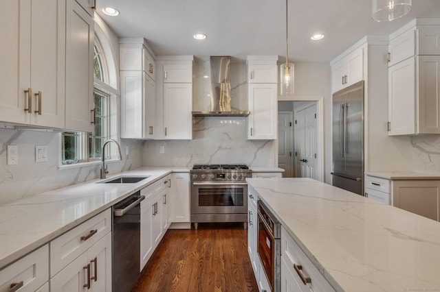 kitchen featuring pendant lighting, sink, white cabinets, high end appliances, and wall chimney exhaust hood