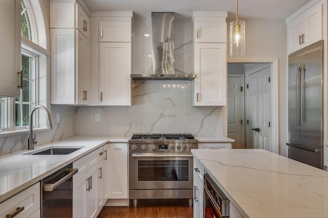 kitchen featuring pendant lighting, wall chimney range hood, sink, high quality appliances, and light stone countertops