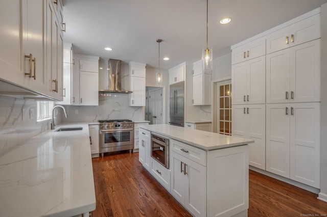 kitchen featuring sink, white cabinetry, built in appliances, a kitchen island, and wall chimney exhaust hood