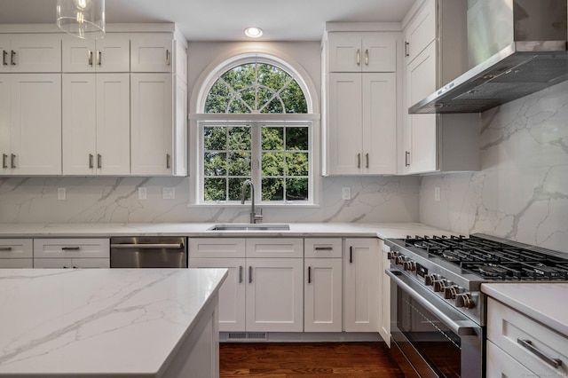 kitchen with wall chimney exhaust hood, sink, white cabinetry, decorative light fixtures, and stainless steel appliances