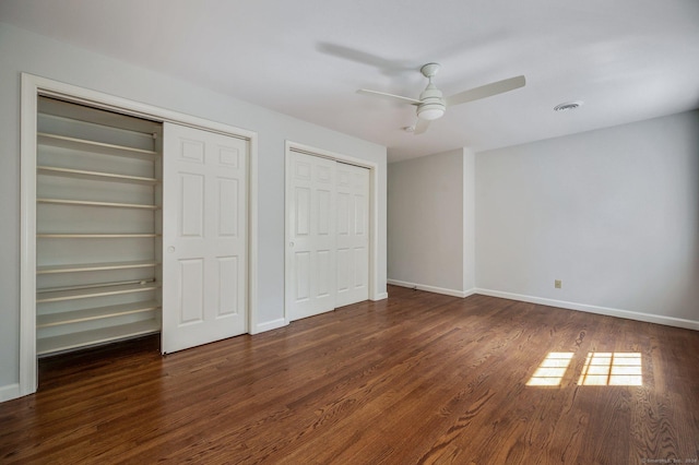 unfurnished bedroom featuring ceiling fan, dark hardwood / wood-style flooring, and two closets