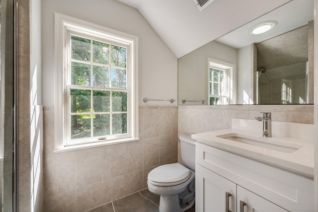 bathroom featuring toilet, vaulted ceiling, tile walls, vanity, and tile patterned flooring