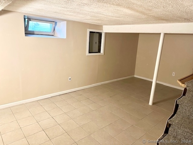 basement with a textured ceiling, electric panel, and light tile patterned floors