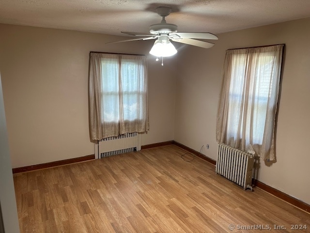 unfurnished room featuring light wood-type flooring, ceiling fan, radiator heating unit, and a textured ceiling