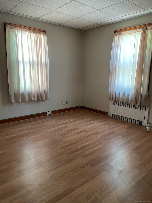 unfurnished room with hardwood / wood-style flooring, a wealth of natural light, radiator, and a drop ceiling