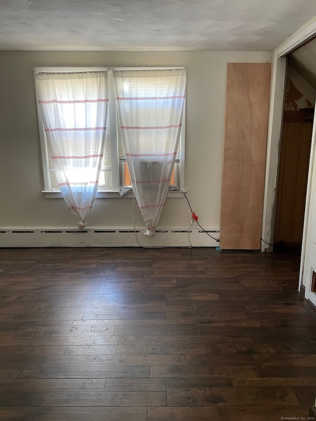 empty room with dark wood-type flooring and a baseboard radiator