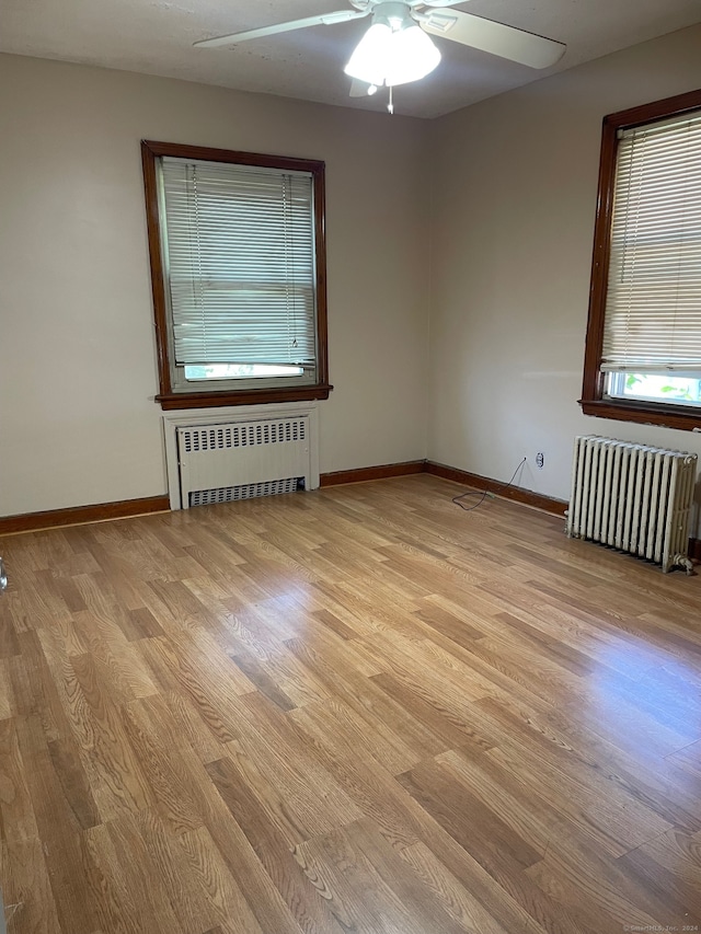 unfurnished room featuring radiator heating unit, light hardwood / wood-style flooring, and ceiling fan