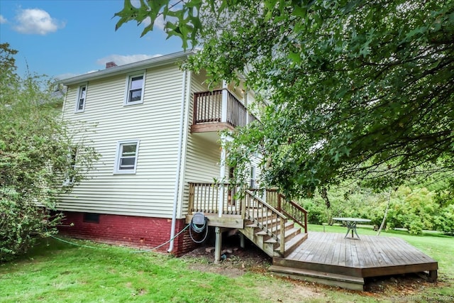 rear view of property featuring a lawn, a balcony, and a wooden deck