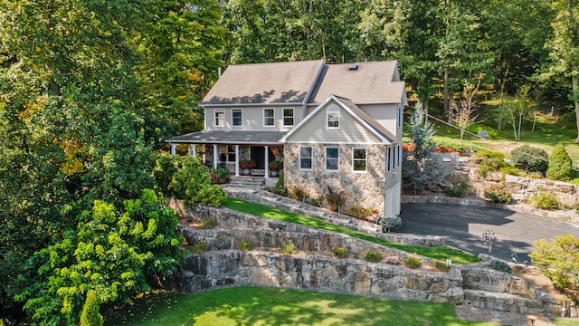craftsman house with a porch, a front lawn, driveway, and stone siding